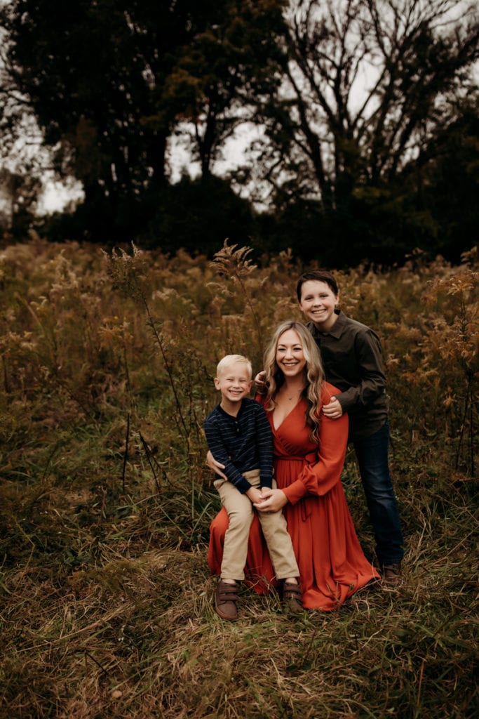Newborn and Maternity Photographer, Evie Lynn kneels with her two boys in a field